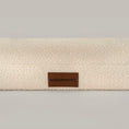 Load image into Gallery viewer, Close-up of the cream bouclé cover and leather BONE & BOWS label on The Lounger