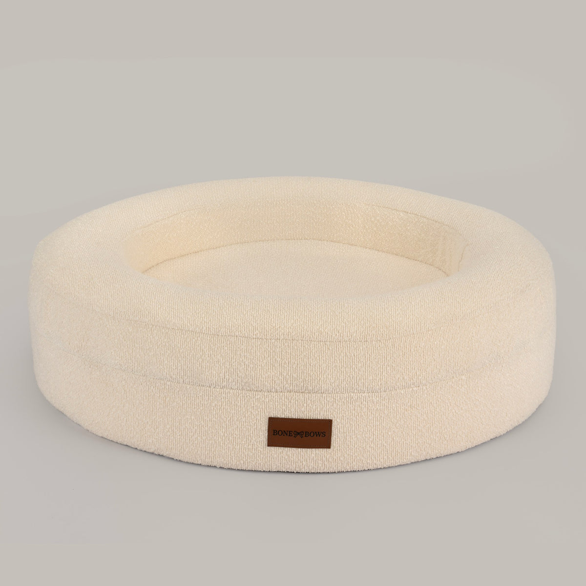 The Cocoon round dog and cat bed in cream bouclé, front view with the leather BONE & BOWS label