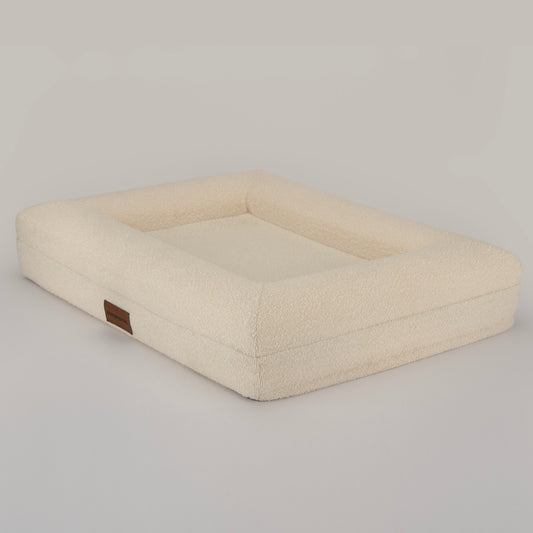 The Lounger in cream bouclé, three-quarter view showing the low bolster edge