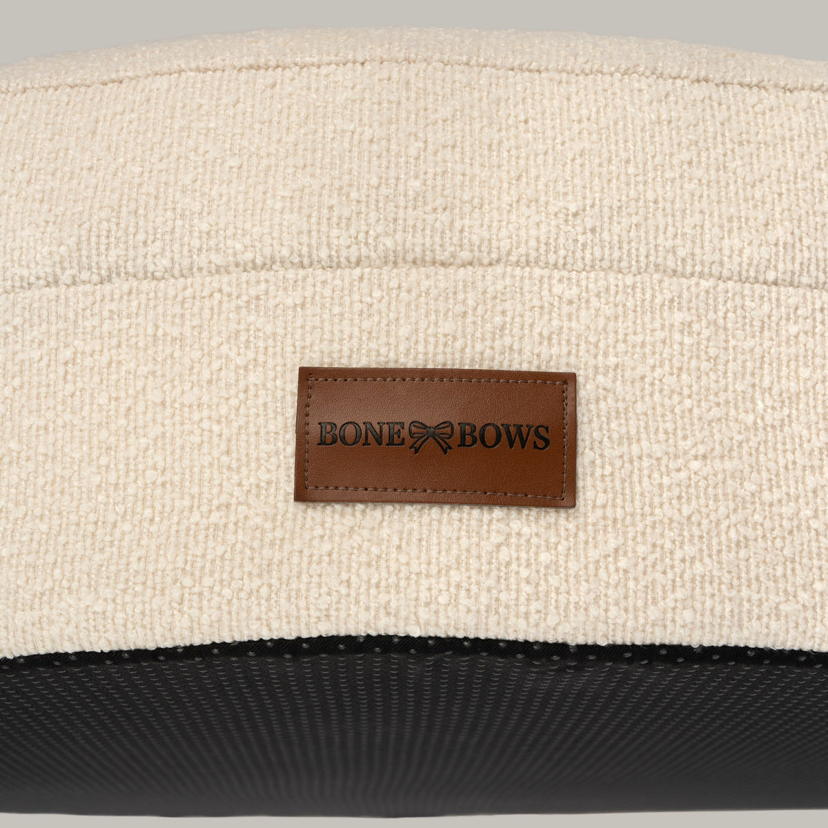 Close-up of the cream bouclé cover and leather BONE & BOWS label on The Cocoon