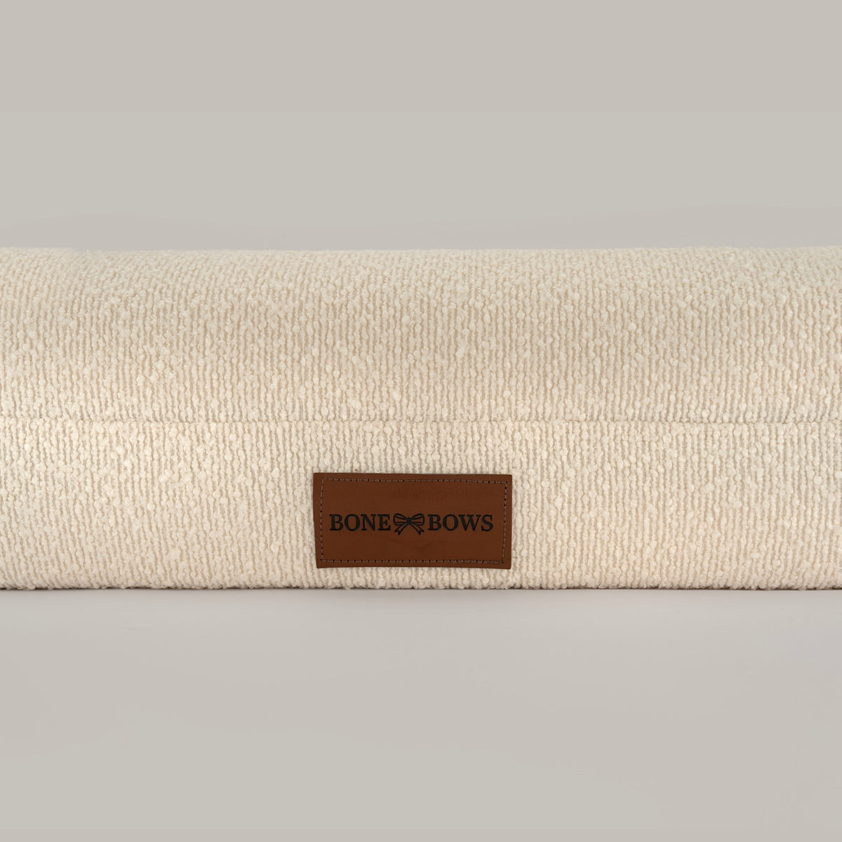 Close-up of the cream bouclé cover and leather BONE & BOWS label on The Lounger